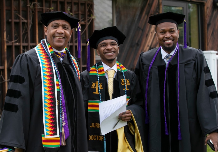 Three men are standing together in graduation attire, smiling proudly.