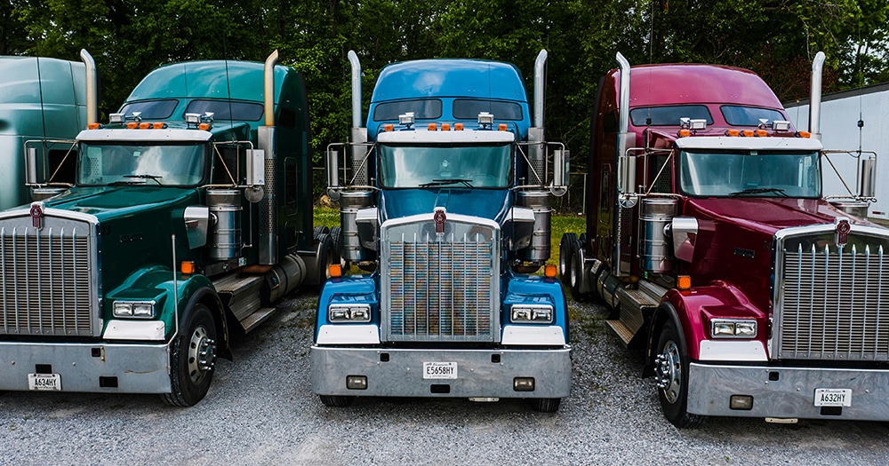 Three large trucks (green, blue, red) facing the camera.